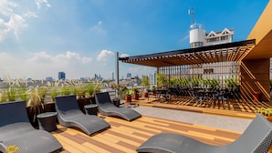 A rooftop lounge with lounge chairs, a pergola, and a city view.