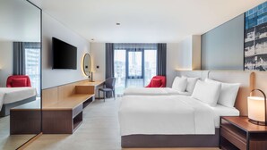 A modern hotel room with a large bed, a desk, a chair, a TV, and a large window with a city view.