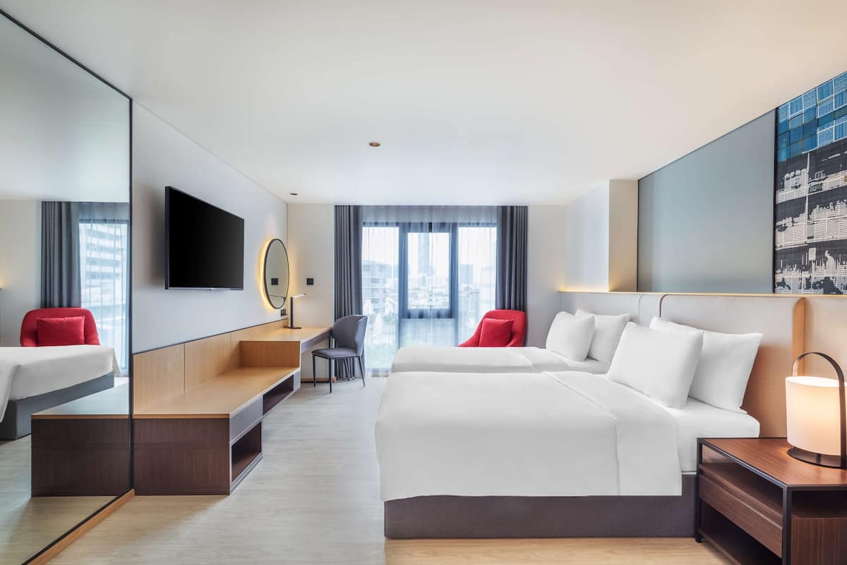 Ein modernes Hotelzimmer mit einem großen Bett, einem Schreibtisch, einem Sessel, einem Fernseher und einem großen Fenster mit Blick auf die Stadt.