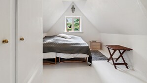 A small, white, attic-style bedroom with a bed, a window, a nightstand, and a wooden table. - 3 bedroom gorgeous home in Nexø (Nexø)