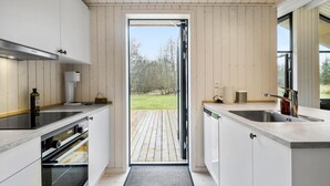 Una cocina moderna con armarios blancos, un lavamanos de acero inoxidable y una terraza de madera que da al exterior.