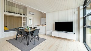 Una sala de estar moderna con comedor, televisor montado en la pared y ventana que deja entrar luz natural.