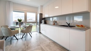 A modern kitchen with white cabinets, a built-in oven, and a large window overlooking a residential area. - Beautiful apartment in Sukosan (Sukosan)