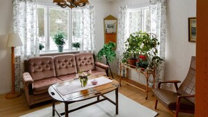 A cozy living room with a sofa, a coffee table, and a chair. There are potted plants and a mirror on the walls.