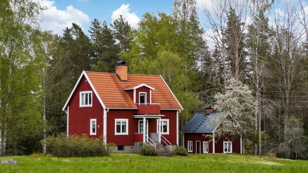 A red wooden house with a sloped roof, a chimney, and a small attached garage.