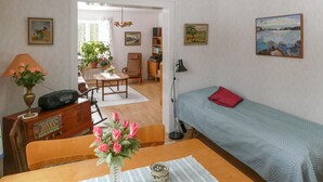A cozy room with a wooden desk, a radio, a vase with flowers, a bed with a blue patterned bedspread, and a bookshelf.