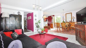Uma sala de estar espaçosa com tapete vermelho, sofá preto e um espaço de jantar com cadeiras e mesa de madeira.