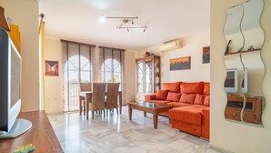 Una sala de estar con un sofá, una mesa de centro y una mesa de comedor. Hay un televisor a la izquierda y un mueble con un espejo a la derecha.