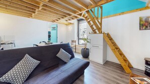 A modern interior with exposed wooden beams, a dark sofa with patterned cushions, a staircase, and a view through a window.