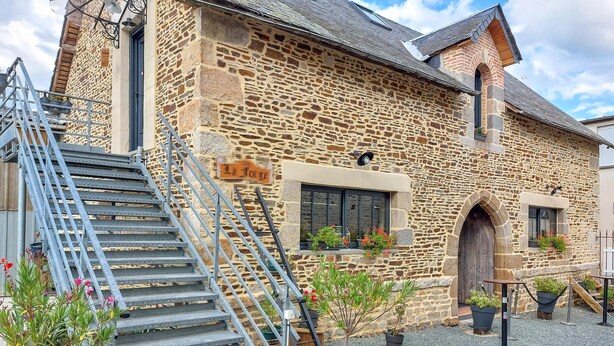 A stone building with a staircase leading to the entrance, a small window with plants, and a door.