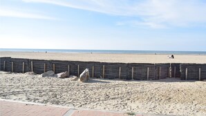 A sandy beach with a wooden fence and large rocks in the foreground.