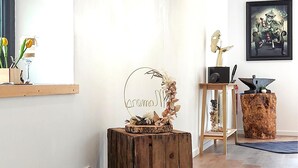 A room with a wooden stool, a decorative sign, a framed artwork, and a shelf with flowers.