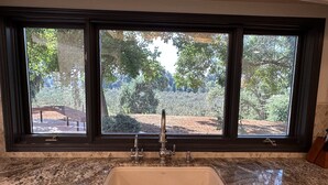 A kitchen with a granite countertop, a white sink, and a window with a view of trees and a bench outside.