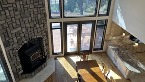 A modern kitchen with a stone fireplace, large windows, and a dining area.