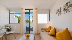 Una sala de estar moderna con un sofá, una mesa de centro con un frutero, un comedor con una mesa y sillas, y vistas a través de un ventanal.