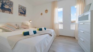 Un dormitorio con una cama, un aparador blanco y dos ventanas con cortinas.
