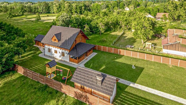 A large house with a sloped roof, surrounded by a wooden fence and a well-maintained lawn.