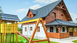 A wooden house with a porch, a swing set, and a small play area.