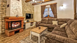 A cozy living room with a stone fireplace, a comfortable sofa, a wooden coffee table, and a television on the wall.