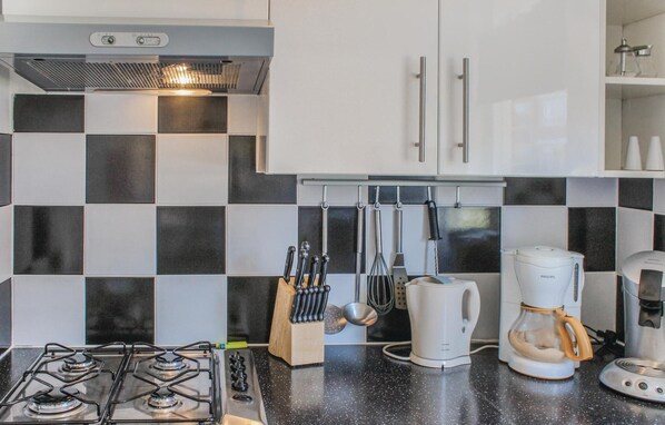 Una cocina moderna con estufa a gas, gabinetes blancos, salpicadero a cuadros blanco y negro, y diversos utensilios y electrodomésticos de cocina.