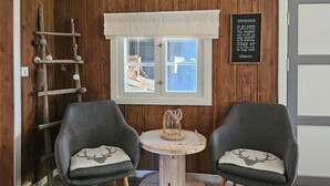 Una stanza accogliente con pareti in legno, una finestra con vista, due poltrone grigie con decorazioni di cervi, un piccolo tavolino e una scala appoggiata al muro.