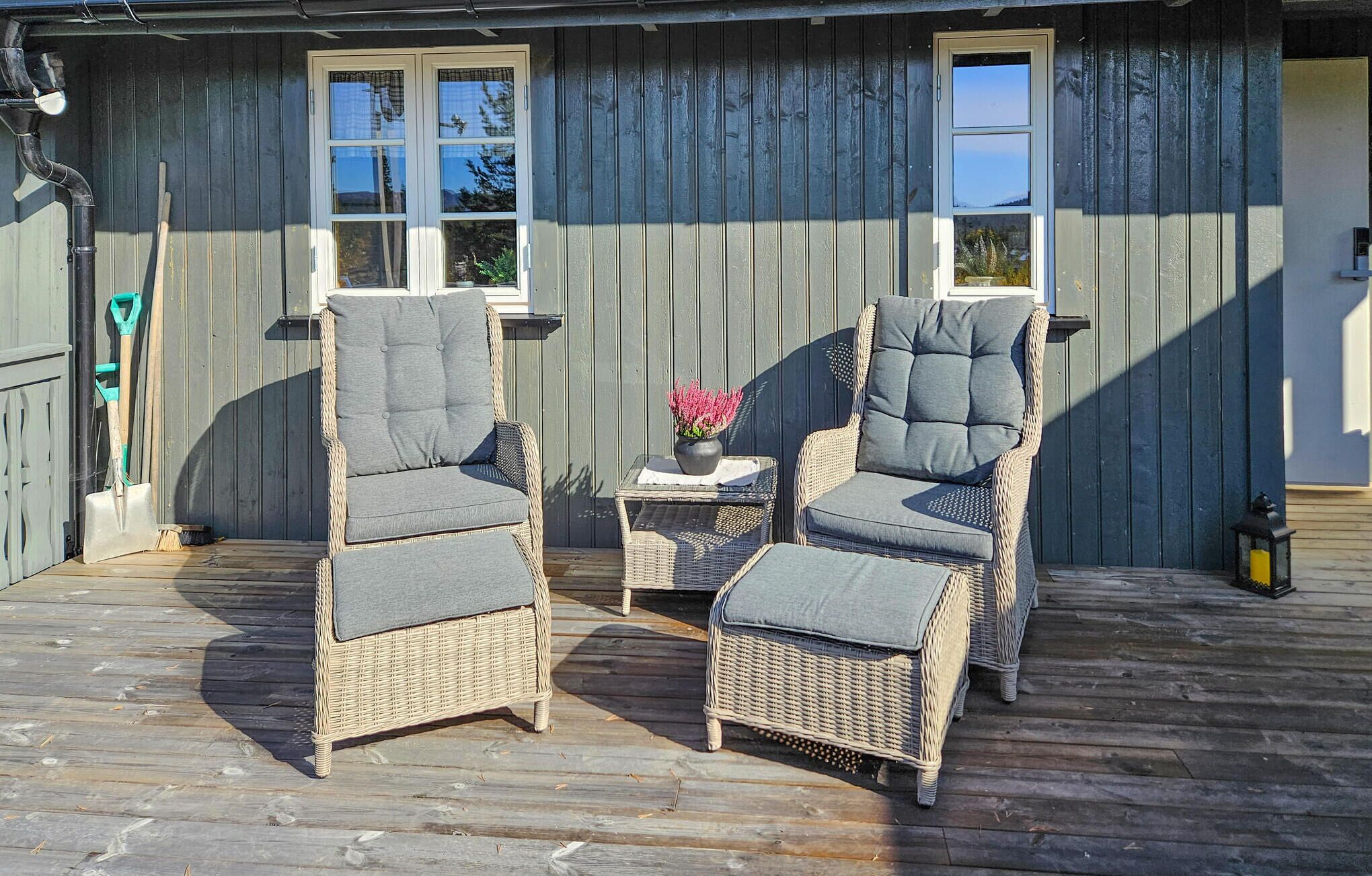 A wooden deck with two wicker chairs and a small table, a potted plant, and a door with windows.