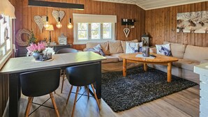 Un accogliente soggiorno con pavimento in legno, un tappeto nero, un divano con cuscini decorati e una zona pranzo con tavolo e sedie.