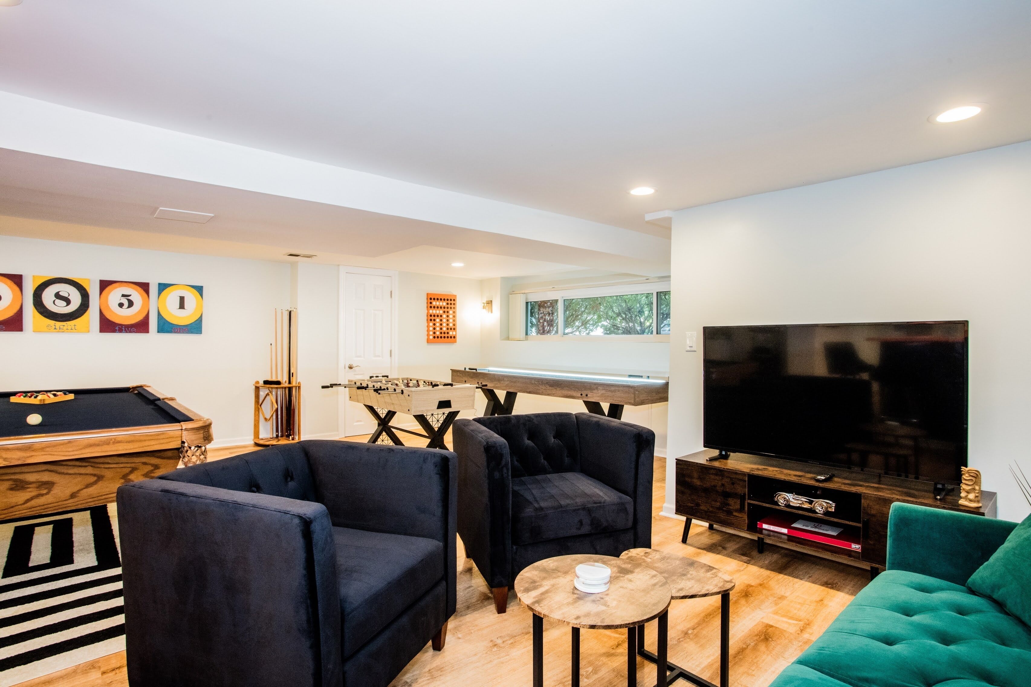 Una sala moderna con mesa de billar, dos sillones, un sofá, televisor y mesa de futbolín.