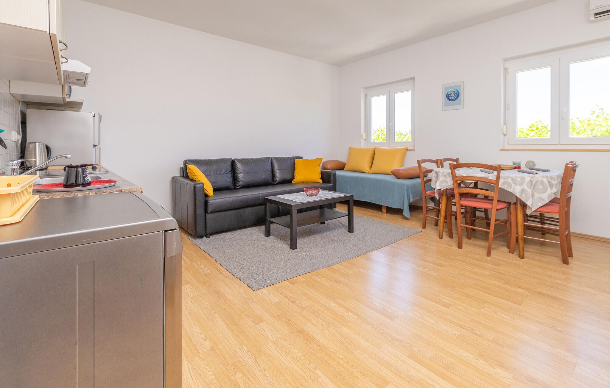 Un espacio habitable compacto con kitchenette, un sofá, una mesa de comedor con sillas y una ventana que proporciona luz natural.
