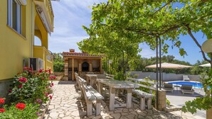 A stone patio with outdoor seating, a pool, and a building with a tiled roof. - Gorgeous apartment in Rab (Rab)