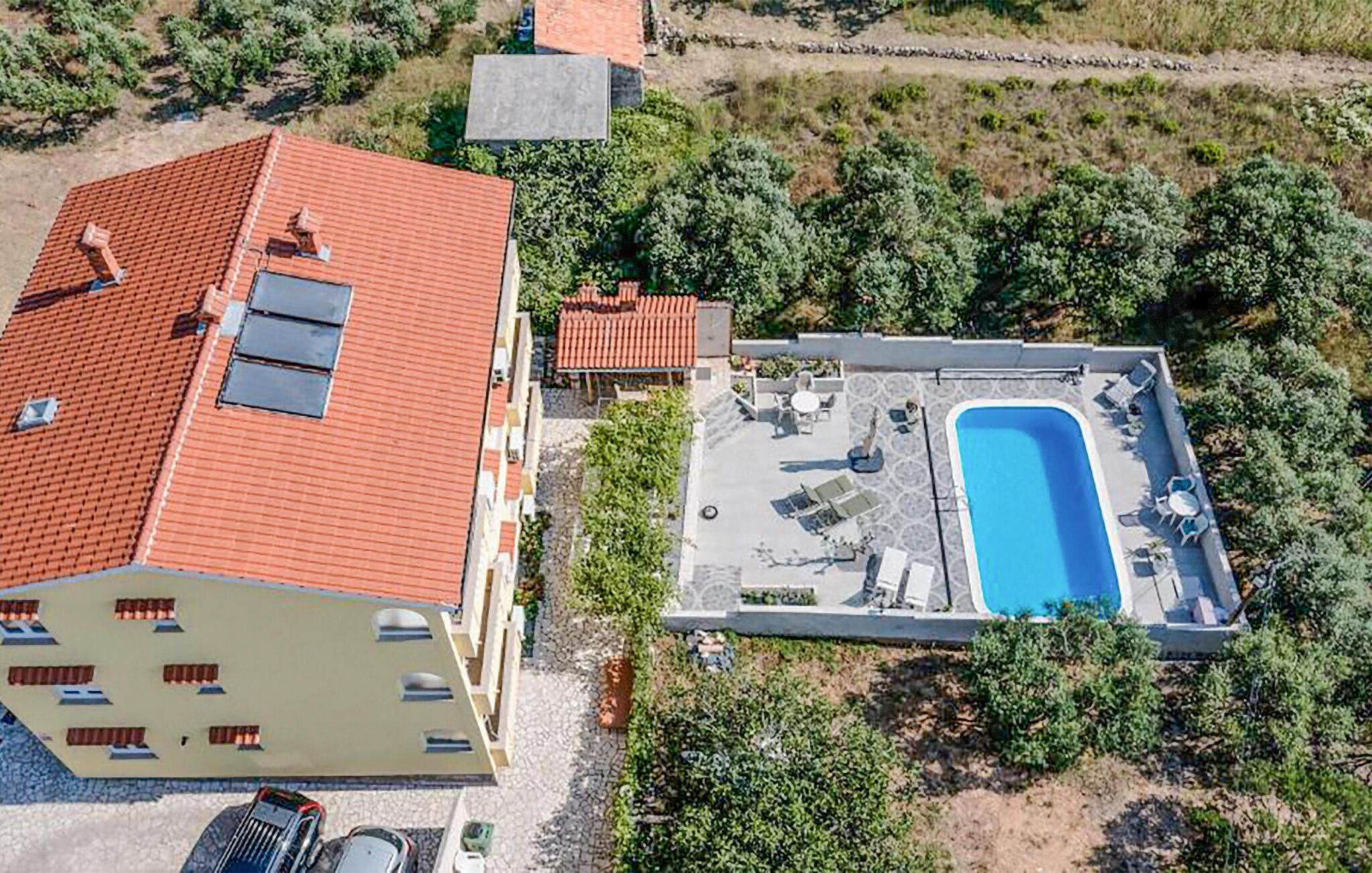 An aerial view of a building with a red-tiled roof, a swimming pool, and surrounding greenery.