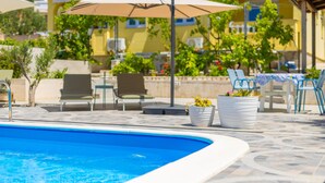 A poolside area with lounge chairs, umbrellas, and potted plants. - Gorgeous apartment in Rab (Rab)