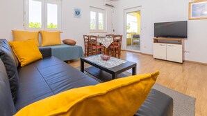 A living room with a sofa, a dining table, chairs, a TV, and a window. - Gorgeous apartment in Rab (Rab)