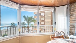 Un balcón con vista a la playa y al océano, una mesa con mantel con motivos de café y una silla de mimbre.