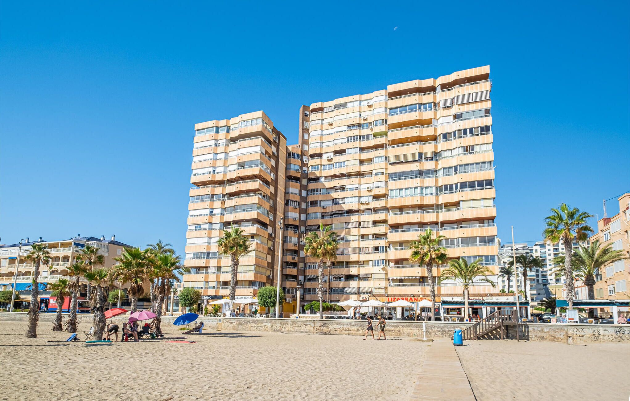 A beachfront hotel with multiple balconies, palm trees, and beachside amenities.
