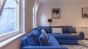 A modern living room with a blue sectional sofa, a floor lamp, and framed artwork on the wall. - Modern, Luxurious 1BR Flat- Heart of Covent Garden (London)