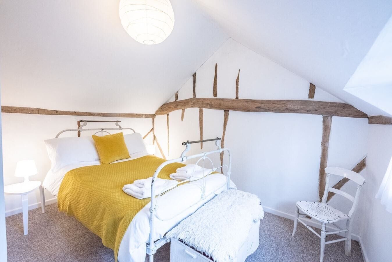 Een slaapkamer met een bed, een stoel, een nachtkastje en een lamp.