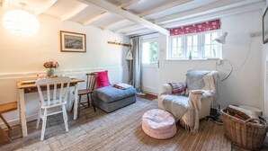 A cozy room with a wooden desk, a chair, a cushioned bench, a fluffy armchair, and a wicker basket. - Lilac Cottage, Wenhaston (Halesworth)