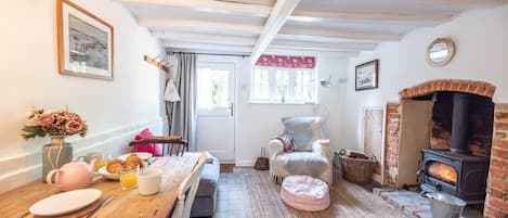 Une pièce chaleureuse avec une table en bois dressée pour le petit-déjeuner, un fauteuil confortable, un petit tapis et une cheminée en briques.