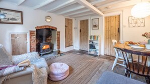 A cozy living room with a fireplace, a dining area with breakfast, and a bookshelf. - Lilac Cottage, Wenhaston (Halesworth)