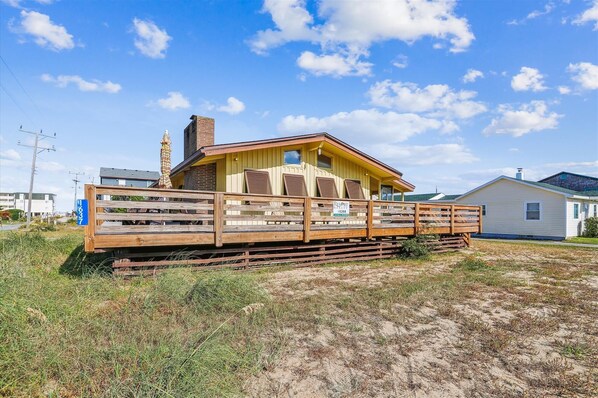 Situated on a sandy area, this cabin features a wooden deck and a small porch with a window.
