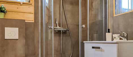 A modern bathroom with a glass shower enclosure, a white sink with a mirror, and a wooden shelf above the sink.