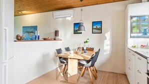 Uma área de refeições com mesa e cadeiras de madeira, uma luminária pendente e uma janela com vista para a paisagem.