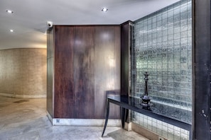 Experience a clean and uncluttered space with a dark paneling wall, glass-tiled section, and sleek metal bench.