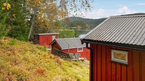 A red wooden cabin with a metal roof, situated on a hillside with a view of a lake and mountains in the background. - Nice home in Follafoss with lake view (Follafoss)