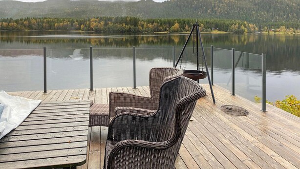 A wooden deck with wicker chairs and a table, overlooking a calm lake with mountains in the background. - Nice home in Follafoss with lake view (Follafoss)
