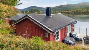 A red cabin with a metal roof, a chimney, and a small porch with a table and chairs. - Nice home in Follafoss with lake view (Follafoss)