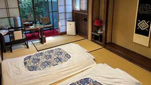 A traditional Japanese room with tatami flooring, a low table with a chair, a bed with patterned bedding, and sliding doors leading to a garden. - Kappo Ryokan Uoichi (Shimada)
