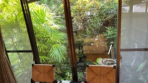 A room with two wicker chairs facing a large window, a small table with a decorative rug, and a view of lush greenery outside. - Kappo Ryokan Uoichi (Shimada)