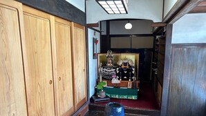A traditional Japanese room with wooden sliding doors, a shrine with a statue, and a large blue vase on the floor. - Kappo Ryokan Uoichi (Shimada)